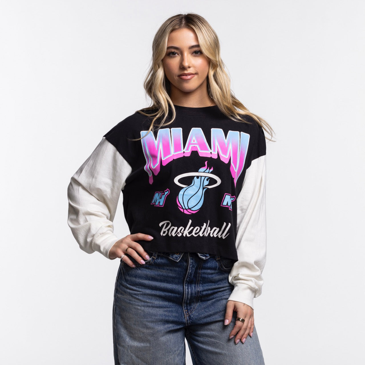 A woman with long blonde hair models the '47 Brand Miami HEAT Original Vice Nights Women's Crewneck in black and white, paired with blue jeans. She stands against a plain white background, hand on hip, showcasing a casual, stylish look.