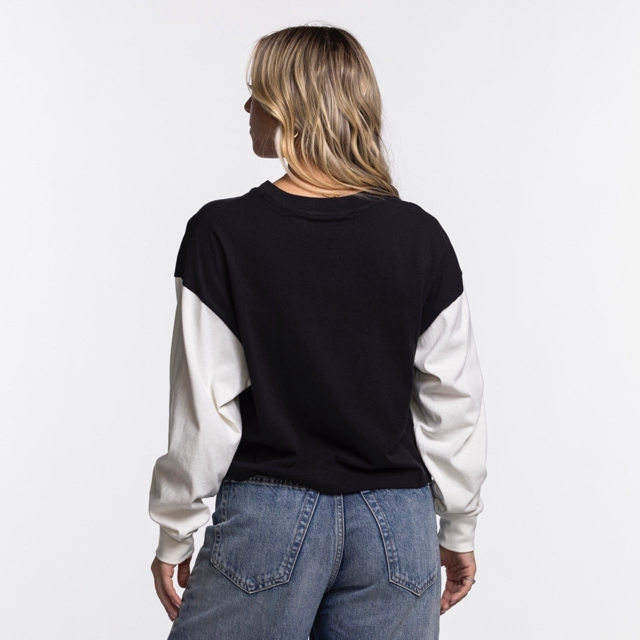 A person with long, wavy blonde hair faces away, wearing a '47 Brand Miami HEAT Original Vice Nights Women's Crewneck and blue jeans against a plain white background.