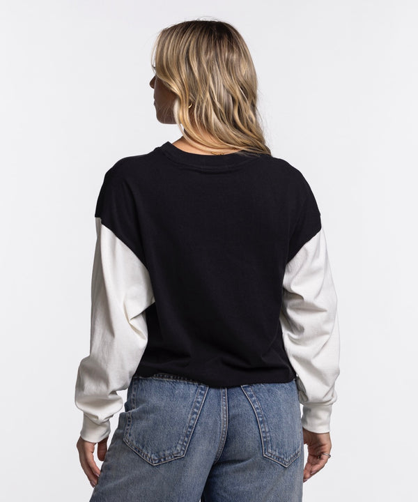A woman with long blonde hair models the '47 Brand Miami HEAT Original Vice Nights Women's Crewneck in black and white, paired with blue jeans. She stands against a plain white background, hand on hip, showcasing a casual, stylish look.