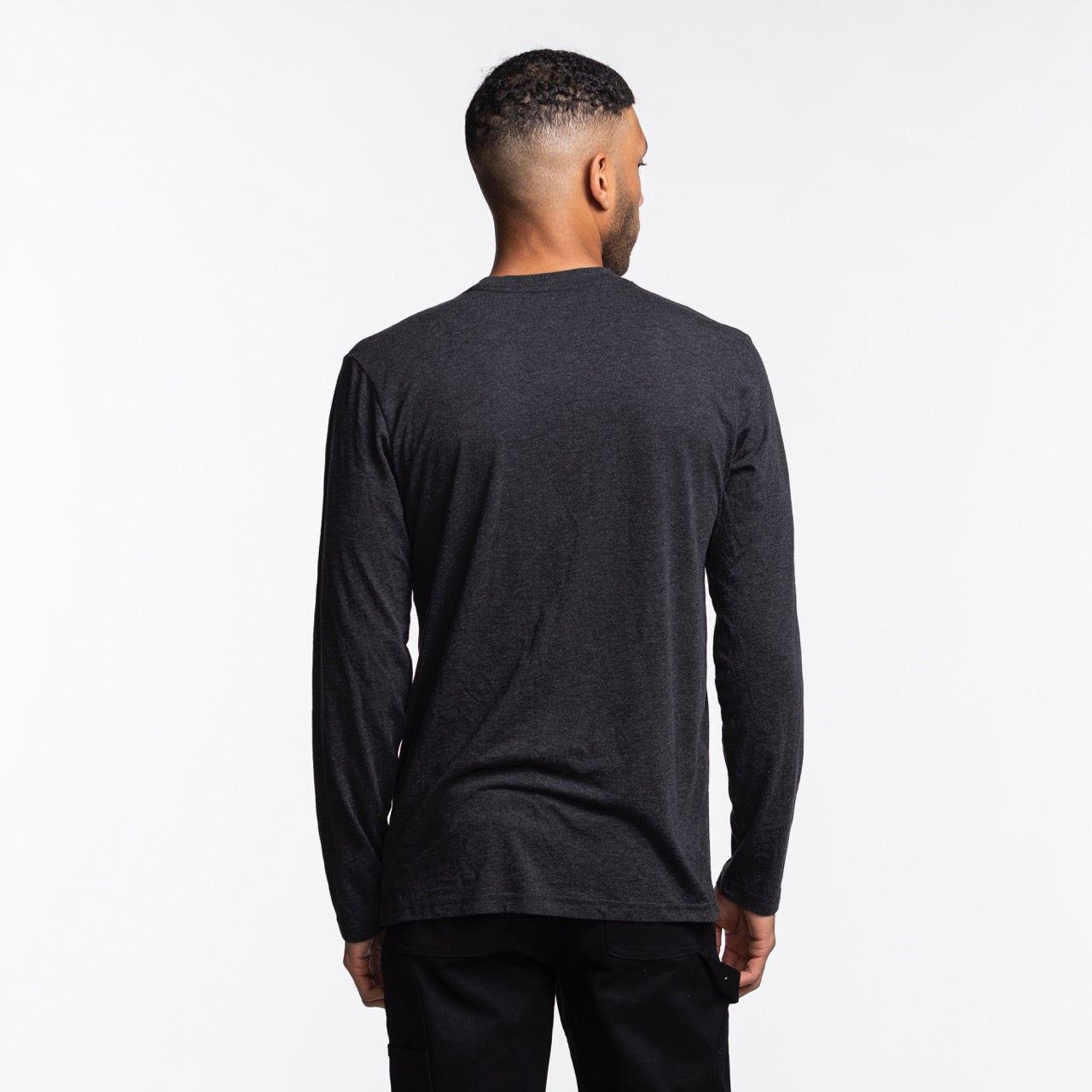 A man with short hair stands with his back to the camera, wearing the Sportiqe Miami HEAT NBA Long Sleeve Tee in dark gray and black pants, against a plain white background. Brand: Sportiqe.
