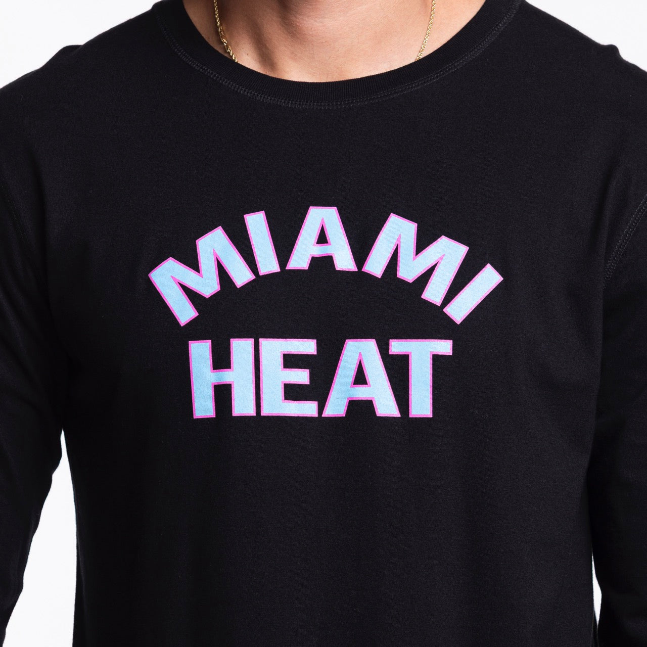 A person wearing a Sportiqe Miami HEAT Original Vice Nights Long Sleeve Tee, featuring a standard fit, black cotton material, 
