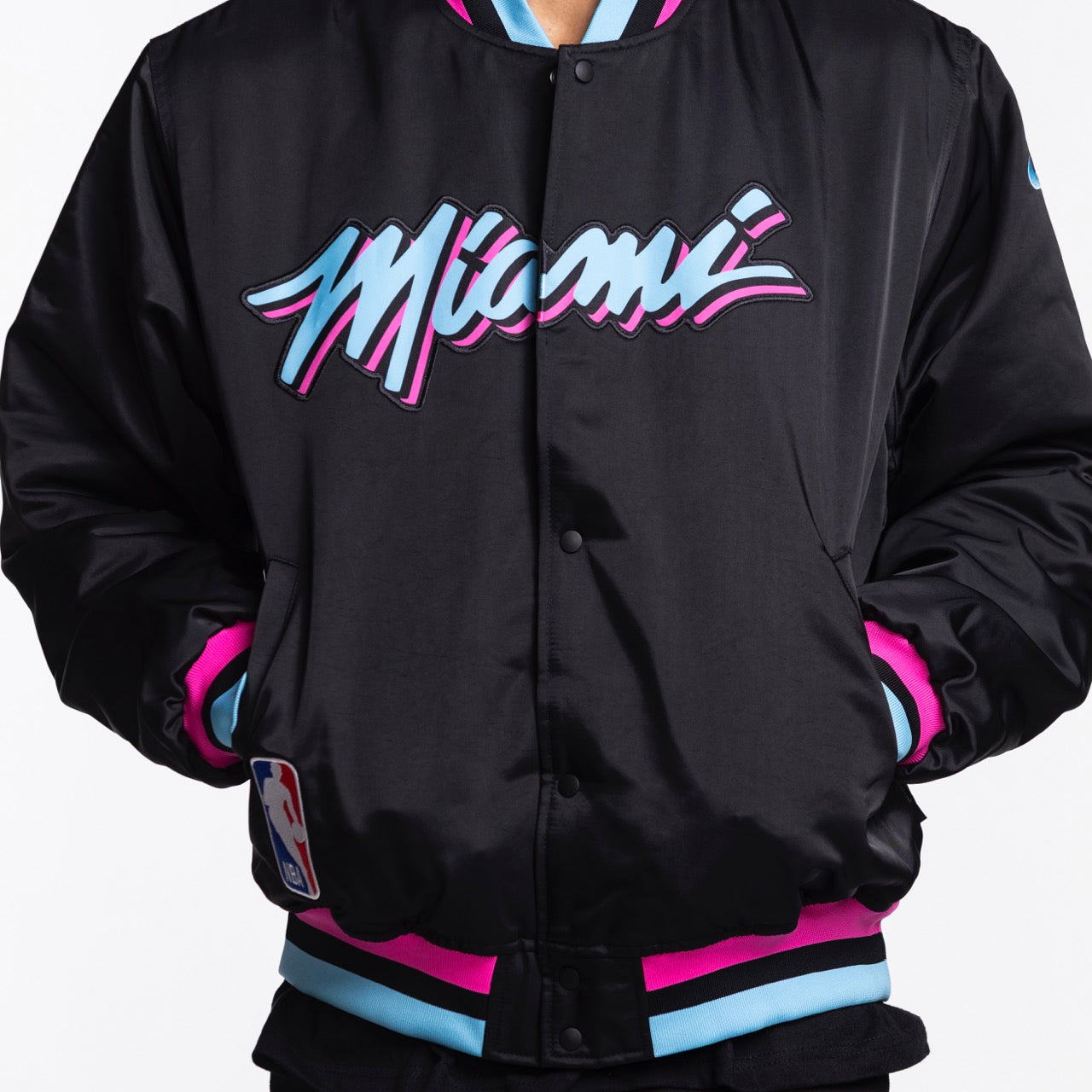 A person wears the Nike Miami HEAT Original Vice Nights Bomber Jacket by Nike—a black insulated varsity jacket with 