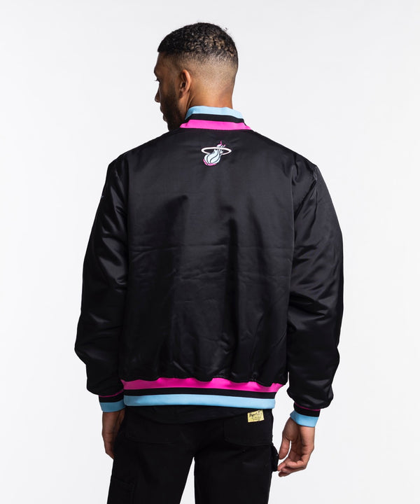 A man wears the Nike Miami HEAT Original Vice Nights Bomber Jacket, a black polyester jacket with 