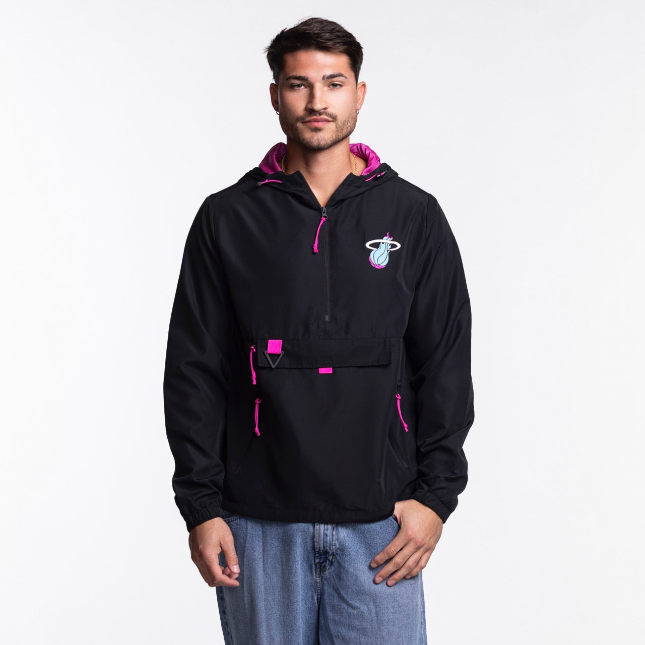 A man wears the Stadium Essentials Miami HEAT Original Vice Nights 1/4 Zip Jacket—black with pink accents and a Miami Heat logo—paired with a polyester hat, standing against a plain white background. One size fits most; spot clean only.