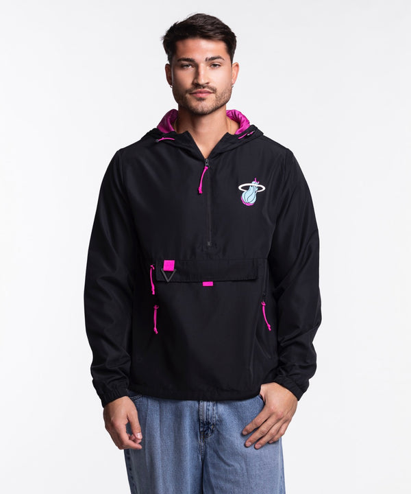 A man wears the Stadium Essentials Miami HEAT Original Vice Nights 1/4 Zip Jacket—black with pink accents and a Miami Heat logo—paired with a polyester hat, standing against a plain white background. One size fits most; spot clean only.