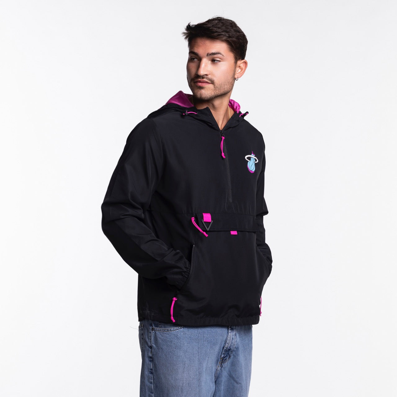 A man models the Stadium Essentials Miami HEAT Original Vice Nights 1/4 Zip Jacket, featuring black with pink accents and a blue-pink chest logo, paired with light blue jeans and a spot-clean polyester hat, all against a white background.