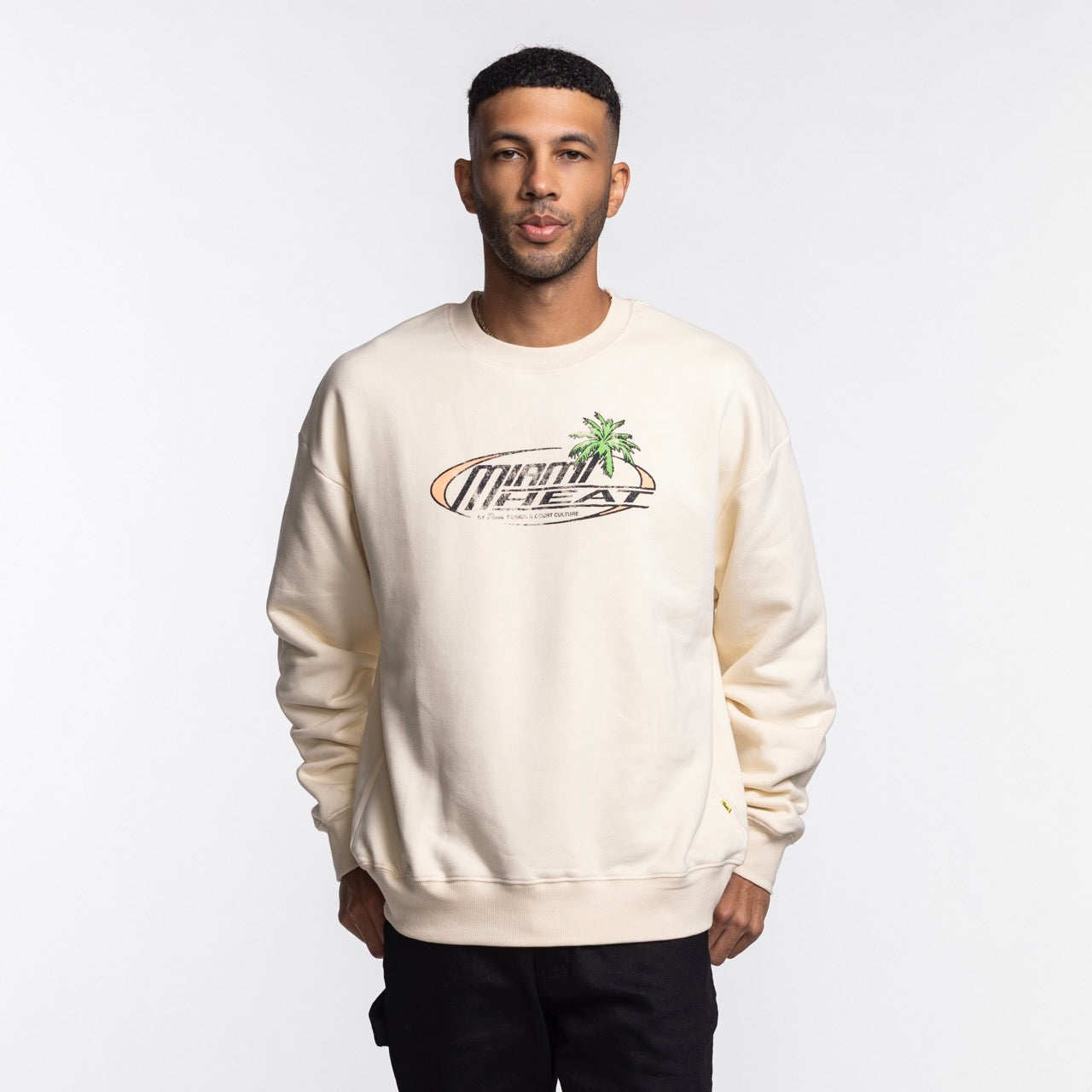 A man with short hair and a trimmed beard wears the Court Culture x Duvin Sun Crew Sweater by Court Culture, featuring Miami Heat text and a palm tree graphic, against a plain white background.
