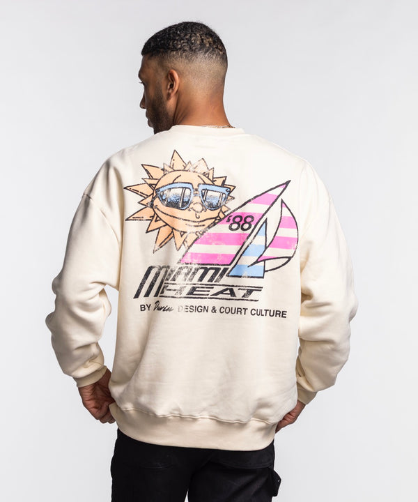 A woman with long blonde hair wears a cream Court Culture x Duvin Sun Crew Sweater and black pants, standing against a plain white background.