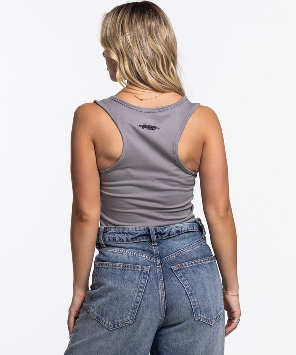 A woman with long blonde hair wears the Pro Standard Miami HEAT Original Vice Nights Women's Tank and blue jeans, standing against a plain white background, looking at the camera with one hand in her pocket.