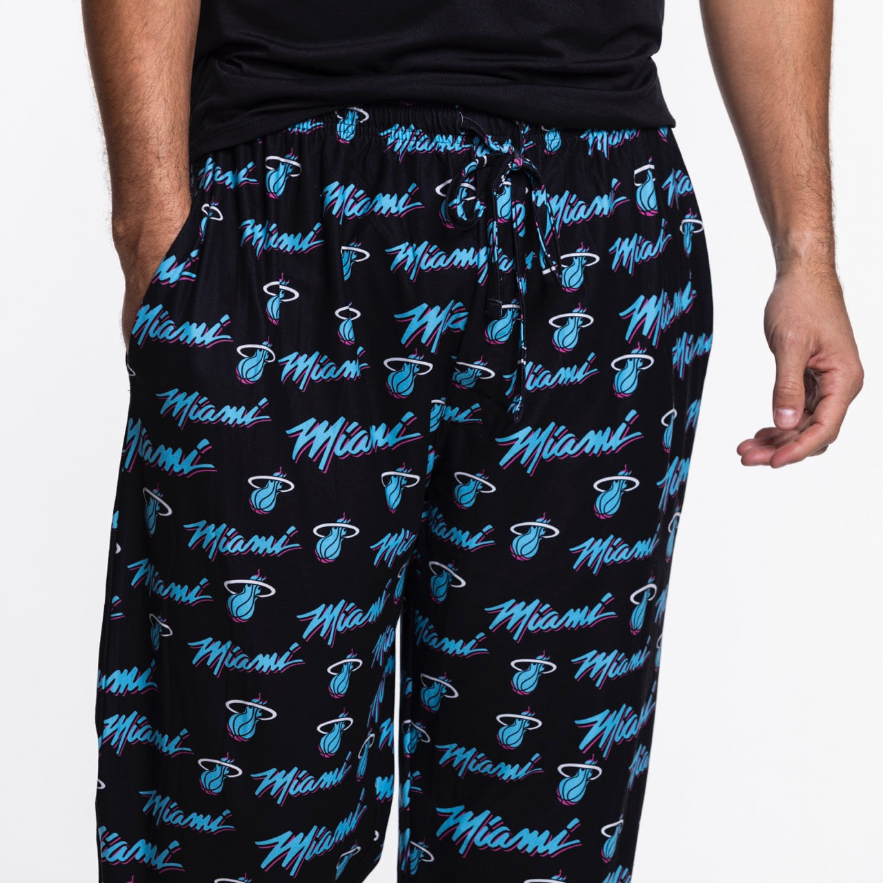 A person wearing Concepts Sports Miami HEAT Original Vice Nights Logo Pants with colorful Miami text and team logos printed all over. Only the lower torso and upper legs are visible.