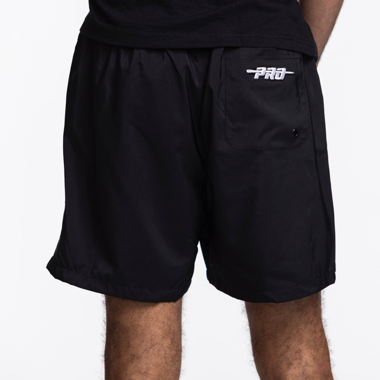 A person wearing Pro Standard Miami HEAT Original Vice Nights Woven Shorts, black polyester with a white PRO logo and front pocket, stands against a plain white background. Only the lower torso and upper legs are visible.