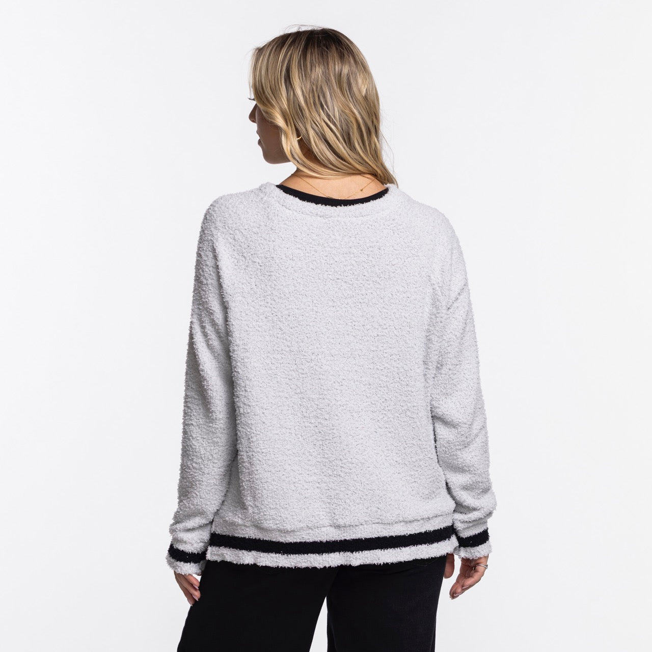 A person with blonde hair is seen from the back wearing the Concepts Sports Miami HEAT Original Vice Nights Women's Crewneck, an oversized fuzzy light gray sweater with black and white striped trim by Concepts Sports, set against a plain white background.