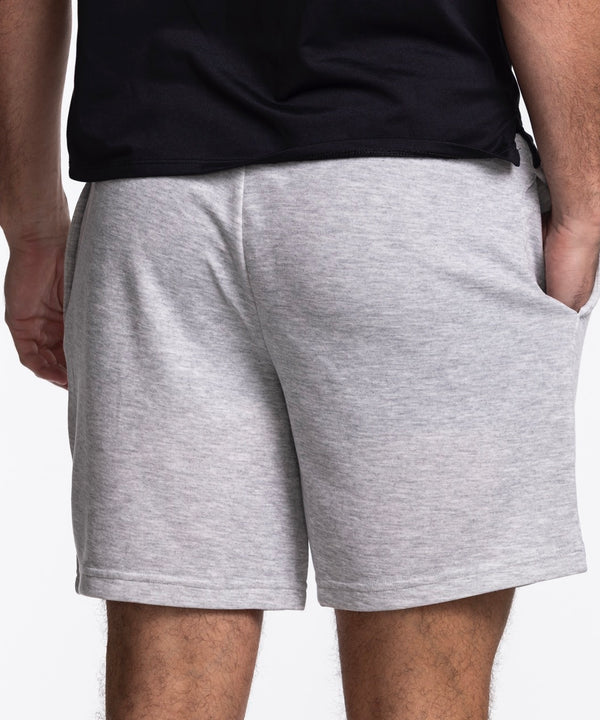 A person wears Concepts Sports Miami HEAT Original Vice Nights Shorts—light gray, relaxed fit with drawstring, hands in pockets—plus a black t-shirt. The polyester cotton shorts have a small round patch of a colorful planet near the hem.
