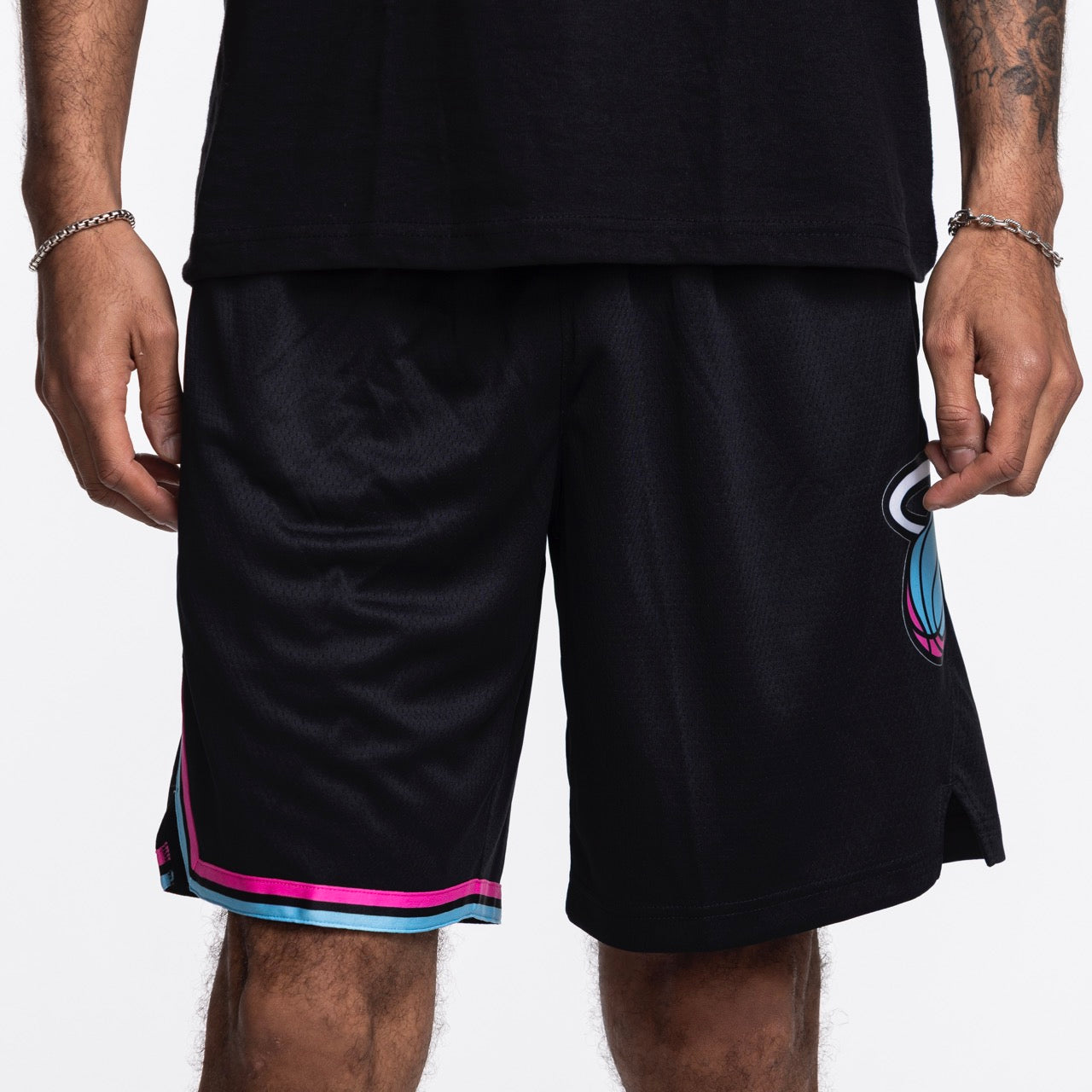 Wearing Nike Miami HEAT Original Vice Nights Swingman Shorts—standard fit black shorts with teal and pink hem stripes, partial team logo on the right leg. Made from polyester; wash with like colors. Paired with a black shirt and silver bracelets.