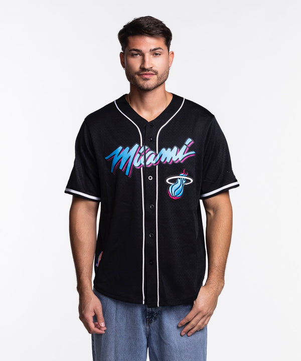A man wearing the Pro Standard Miami HEAT Original Vice Nights Baseball Jersey, featuring colorful Miami text and team logo on the front, stands against a plain white background.
