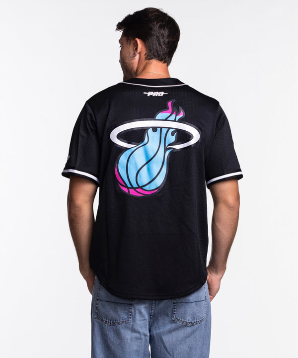 A man wearing the Pro Standard Miami HEAT Original Vice Nights Baseball Jersey, featuring colorful Miami text and team logo on the front, stands against a plain white background.