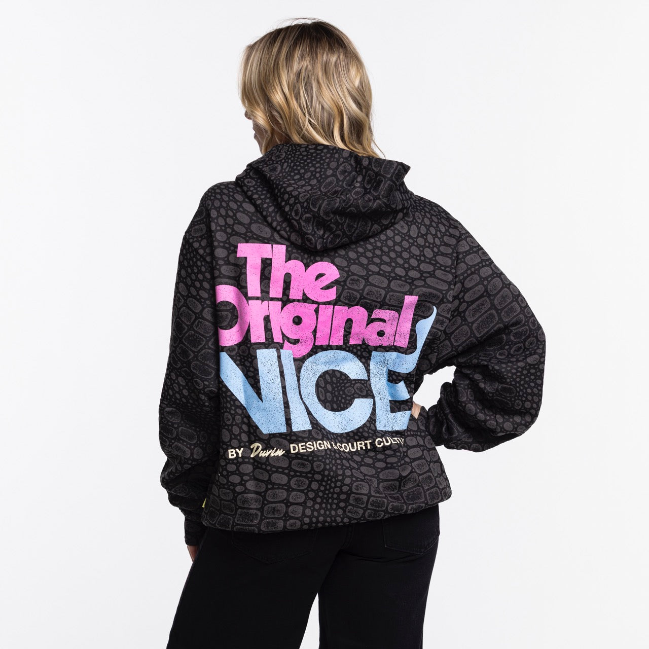 A person with blonde hair faces away, wearing a black Court Culture x Duvin Original Vice Hoodie by Court Culture. The hoodie has a textured pattern and colorful back text: The Original NICE BY Darwin DESIGN COURT COUNTY. Background is plain white.