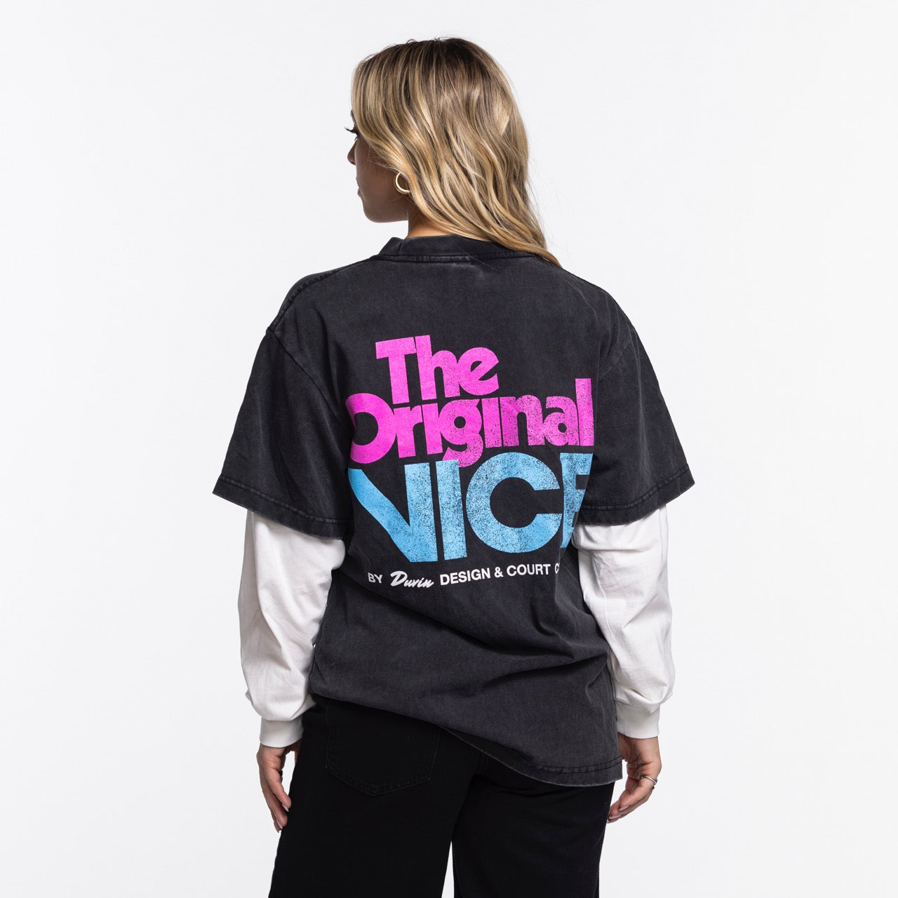 A person with long blonde hair faces away, wearing the Court Culture x Duvin Original Vice Long Sleeve Tee by Court Culture, featuring bold pink and blue 