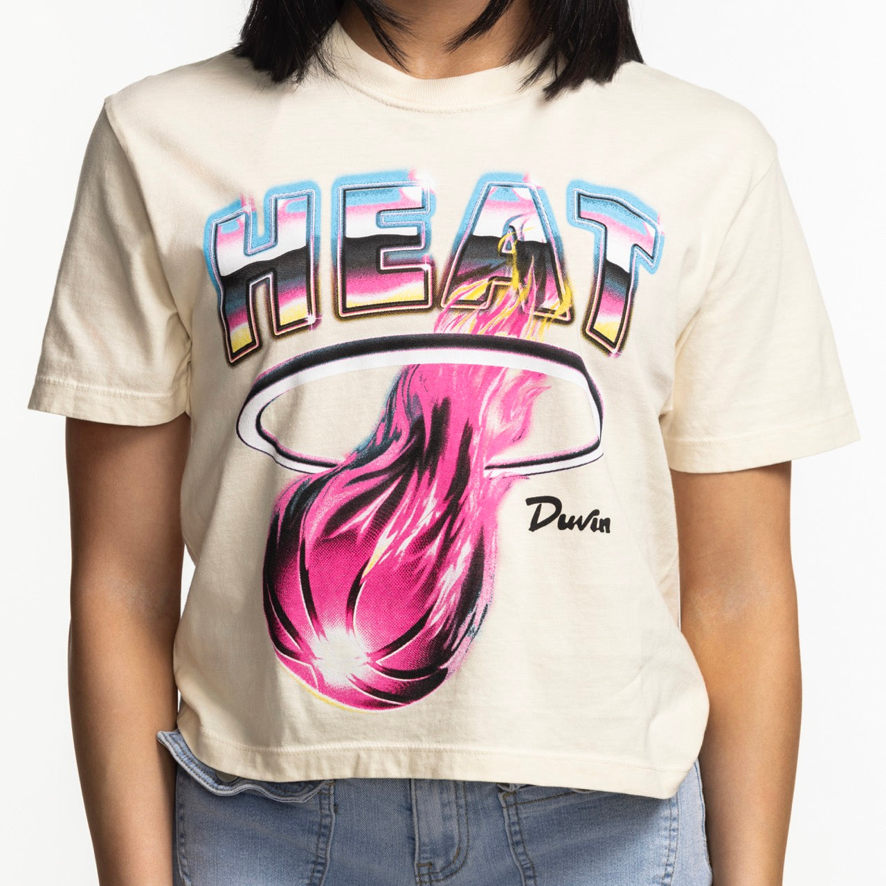 A person wearing the Court Culture x Duvin Tropical Crop by Court Culture, featuring HEAT in bold letters above a flaming basketball and Duvin’s signature, paired with light blue jeans.