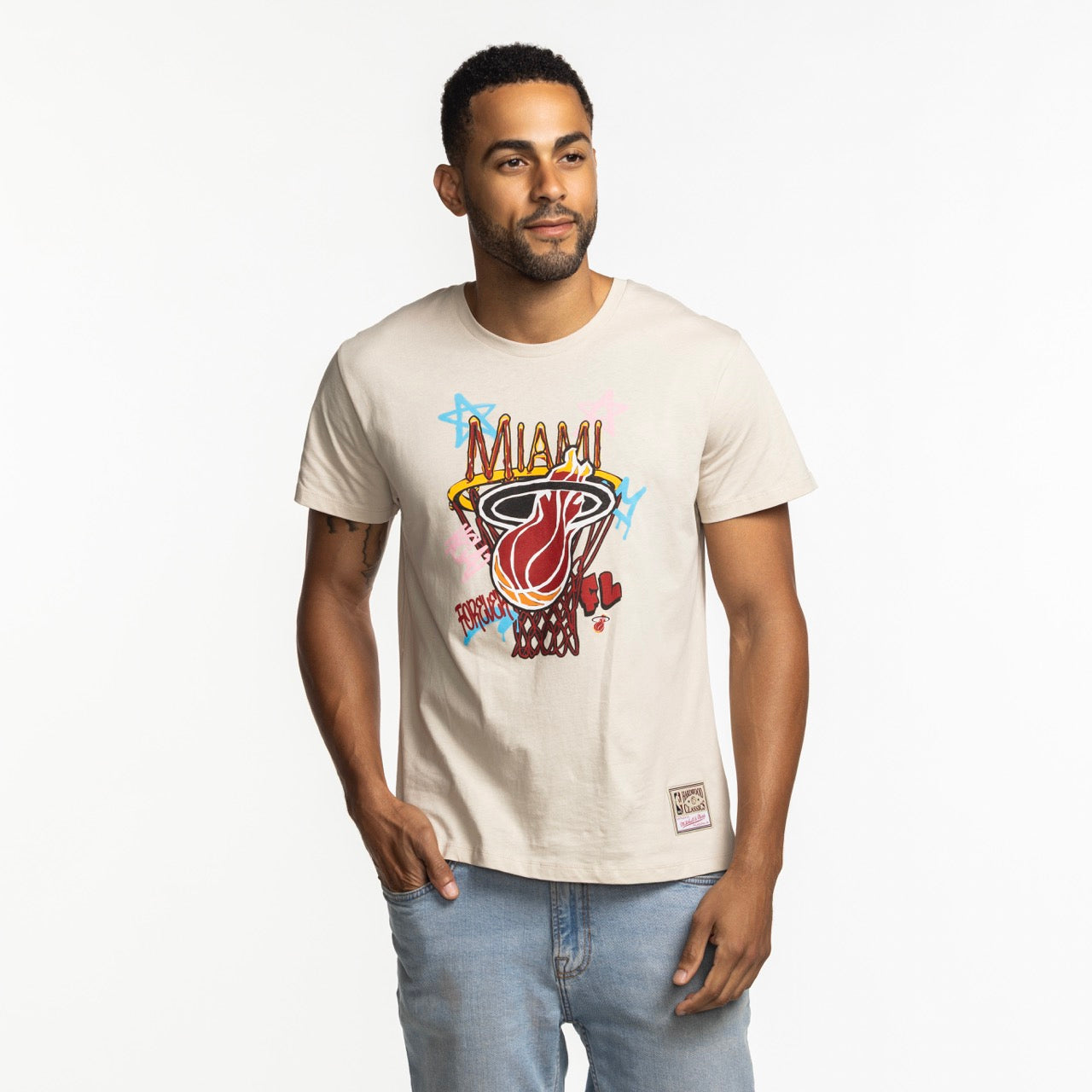 A man stands against a white background wearing the Mitchell & Ness Miami HEAT City Dreams Boxy Tee, made from soft cotton with a standard fit. He has one hand in his pocket and looks slightly to the side.