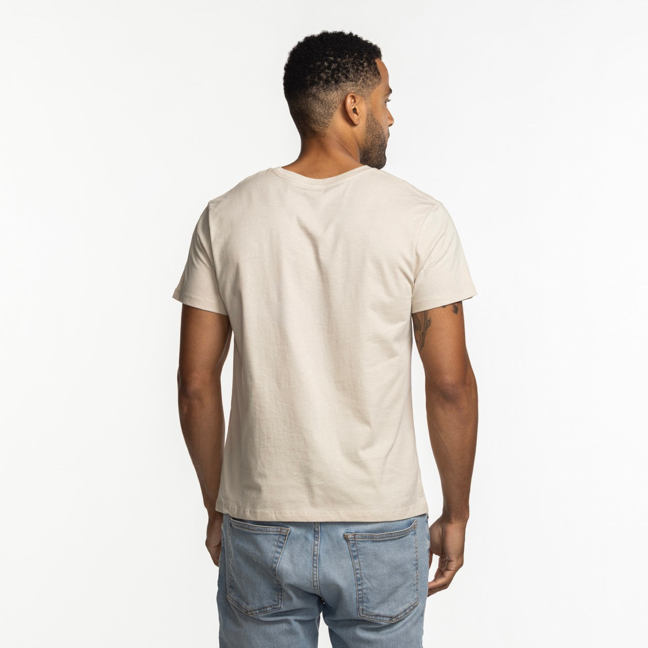 A man wearing a Mitchell & Ness Miami HEAT City Dreams Boxy Tee and light blue jeans stands facing away from the camera against a plain white background.