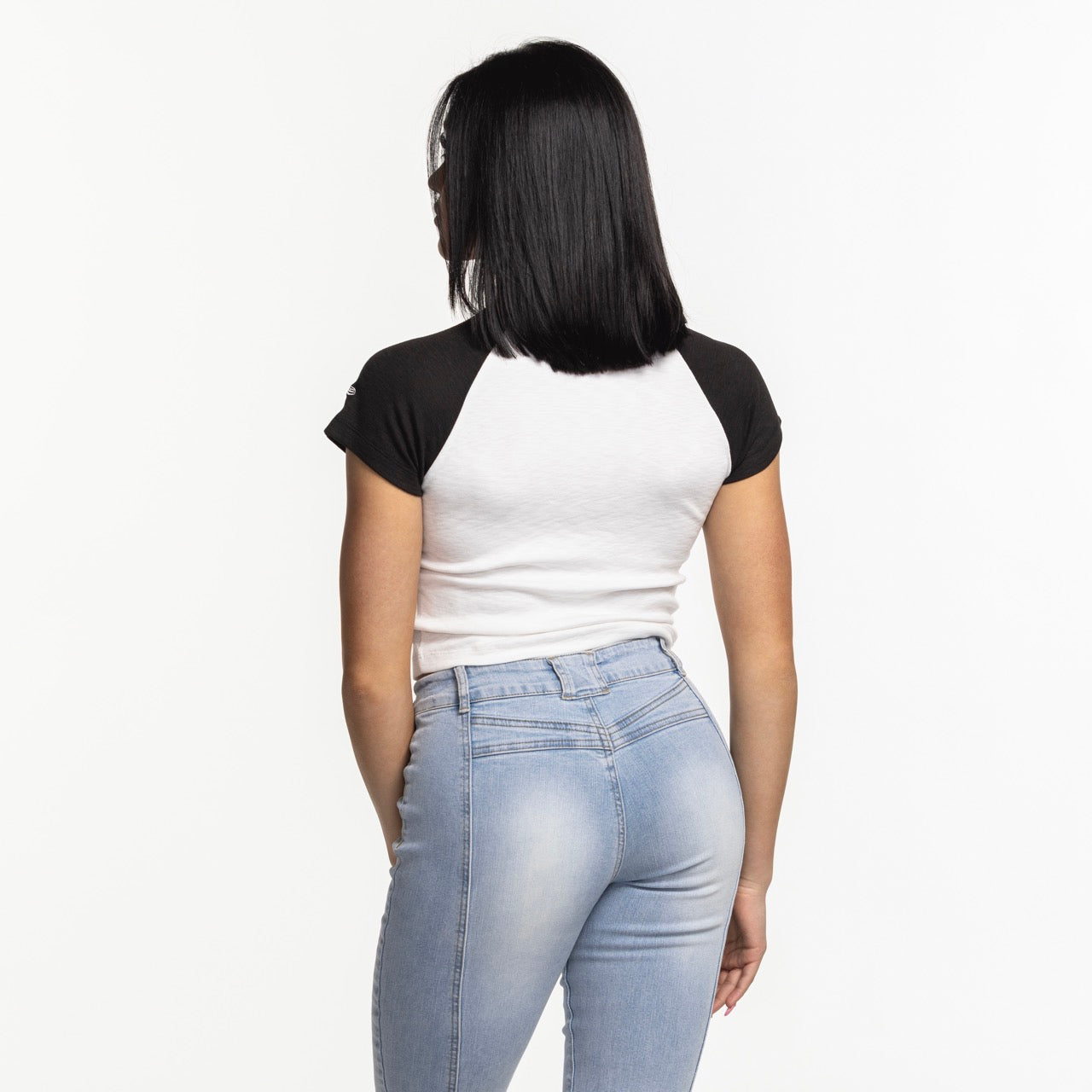 A woman with straight black hair, wearing the New Era Miami HEAT Original Vice Women's Raglan Tee by New Era and light blue jeans, stands facing away from the camera against a plain white background.