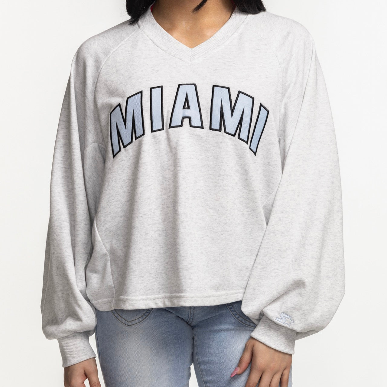 A woman wears the G-III Miami HEAT Faceoff Women's Crewneck by G-III Sports—a relaxed fit, light gray sweatshirt with bold 