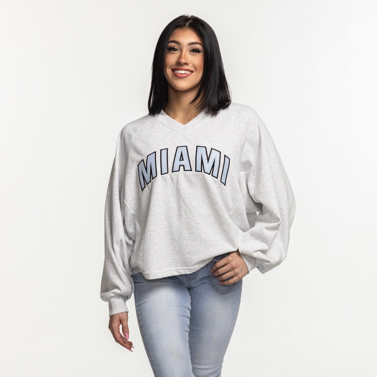 A woman with straight black hair smiles in a G-III Miami HEAT Faceoff Women's Crewneck by G-III Sports—a relaxed fit, light gray cotton-polyester sweatshirt with 