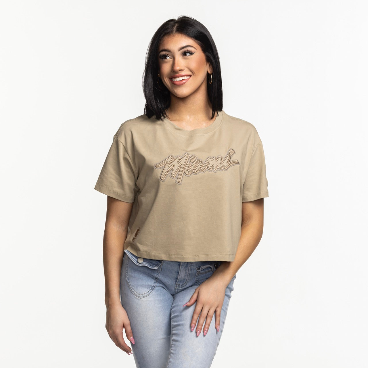 A woman with straight dark hair smiles while wearing the Pro Standard Miami HEAT Original Vice Nights Beige Women's Boxy Tee and light blue jeans, standing against a plain white background.