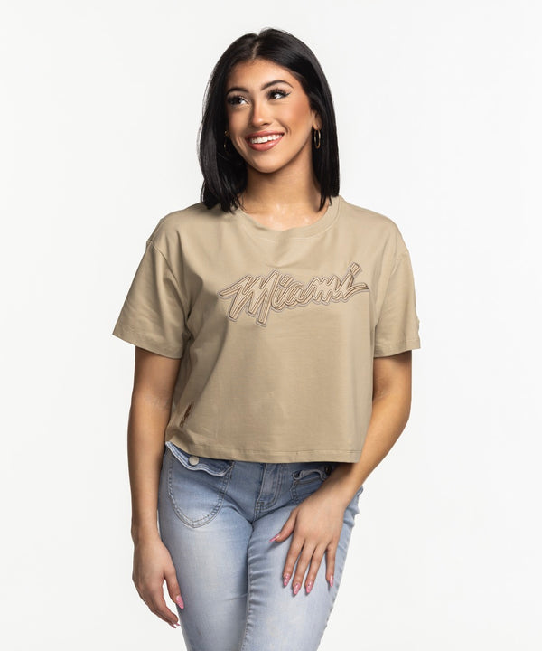 A woman with straight dark hair smiles while wearing the Pro Standard Miami HEAT Original Vice Nights Beige Women's Boxy Tee and light blue jeans, standing against a plain white background.