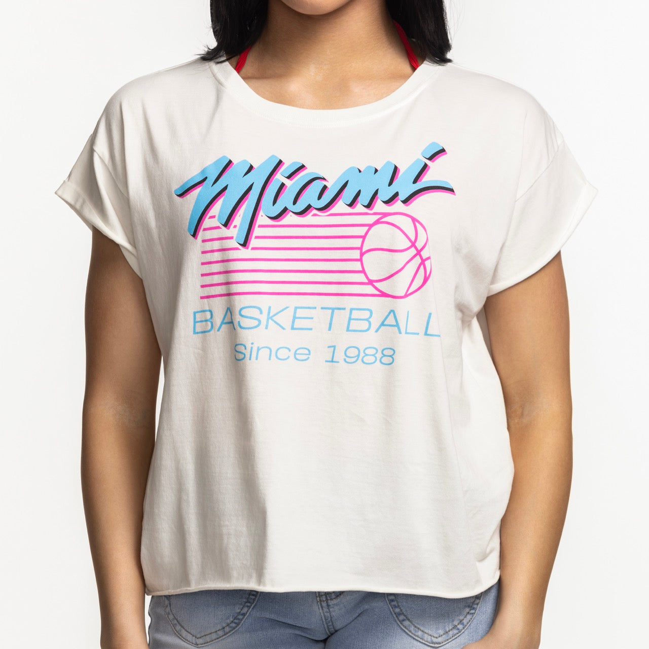 A woman wears the Sportiqe Miami HEAT Original Vice Nights Alana Women's Tee, a relaxed fit cotton top with rolled sleeves and a blue and pink Miami Basketball Since 1988 graphic. This stylish Sportiqe shirt is machine washable.