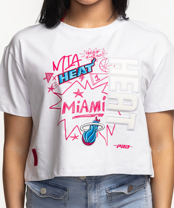 Smiling woman with straight dark hair wearing a Pro Standard Miami HEAT Original Vice Women's Boxy Tee and light blue jeans, standing against a plain white background.