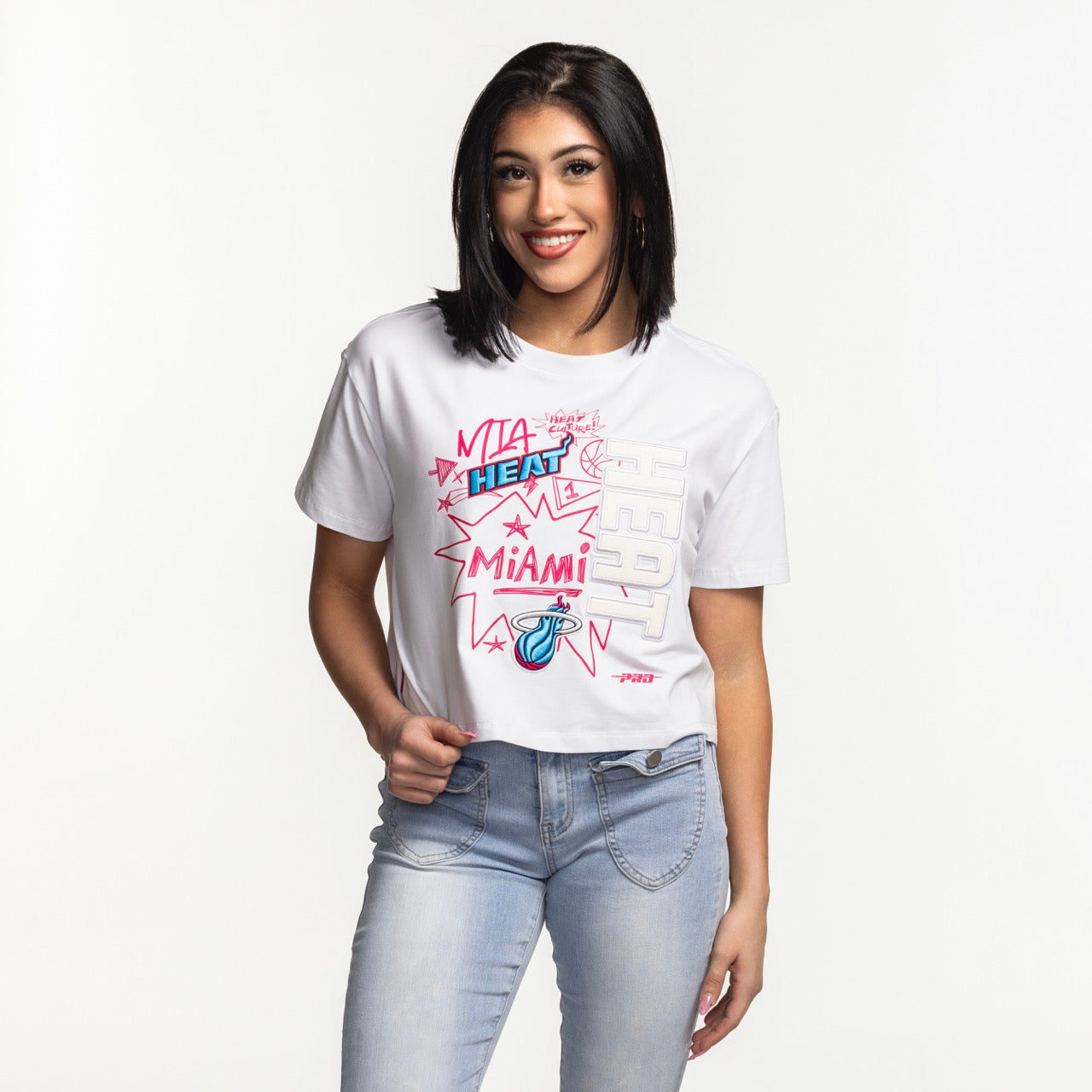 Smiling woman with straight dark hair wearing a Pro Standard Miami HEAT Original Vice Women's Boxy Tee and light blue jeans, standing against a plain white background.