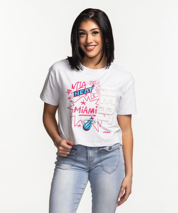 Smiling woman with straight dark hair wearing a Pro Standard Miami HEAT Original Vice Women's Boxy Tee and light blue jeans, standing against a plain white background.