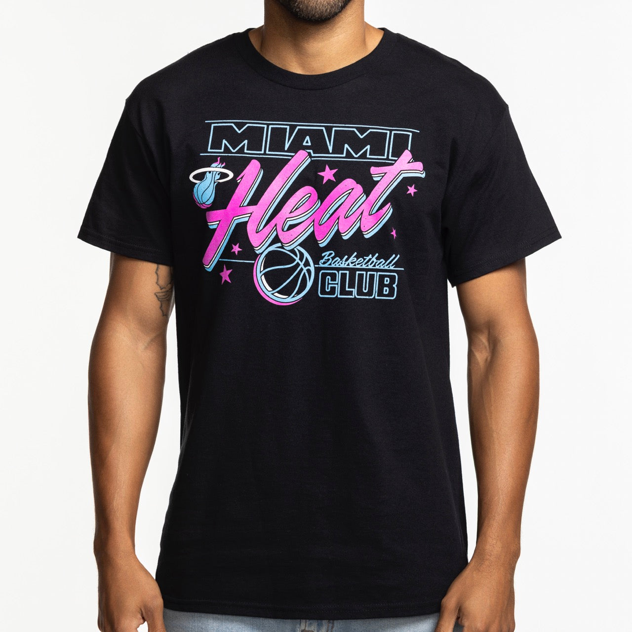 A person wears the Miami HEAT Original Vice Nights Basketball Club Tee by Item Of The Game—a black 100% cotton shirt with a blue, pink, and white Miami Heat design featuring stars and a basketball. Machine washable for easy care.