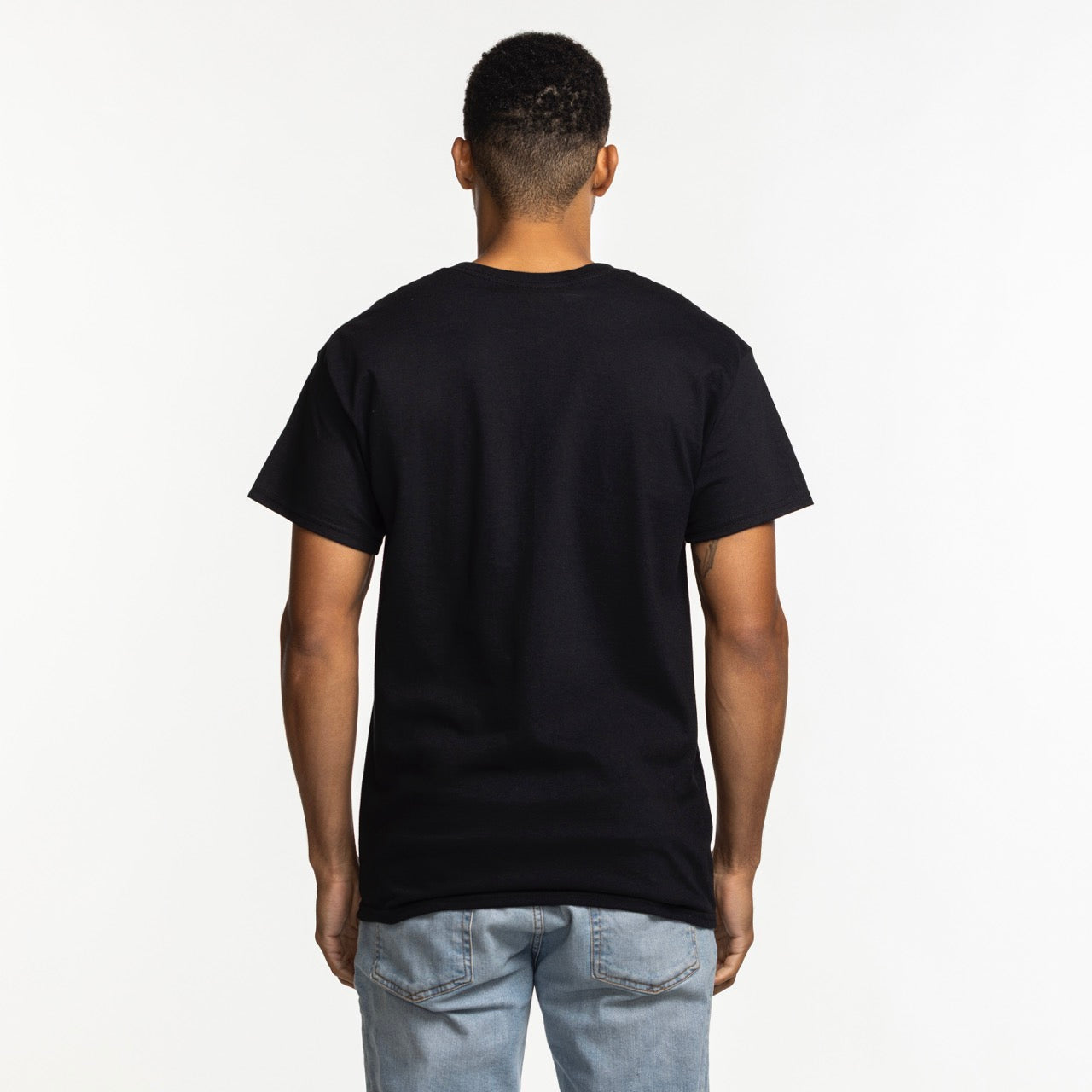 A person with short hair stands with their back to the camera, wearing a standard fit, 100% cotton Miami HEAT Original Vice Nights Basketball Club Tee by Item Of The Game and light blue jeans against a white background.