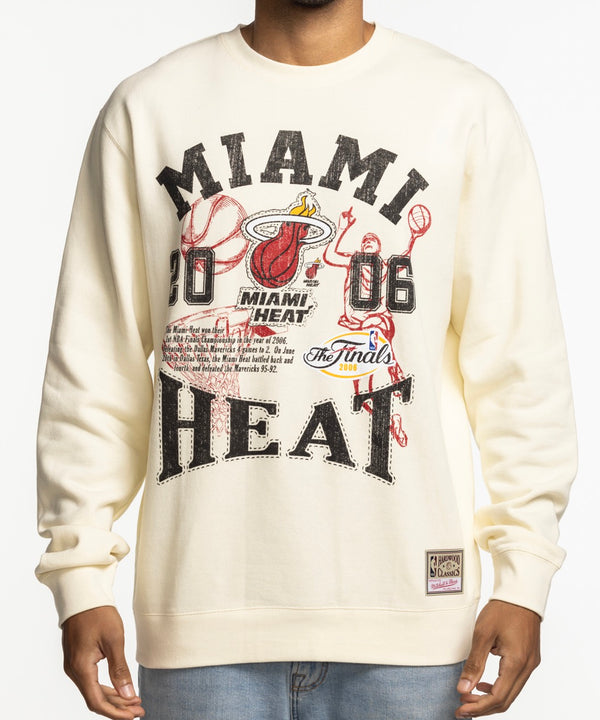 A man smiles against a plain white background, wearing the Mitchell & Ness Miami HEAT 2006 Championship Crewneck by Mitchell & Ness.