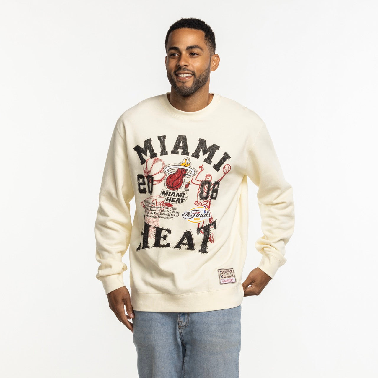 A man smiles against a plain white background, wearing the Mitchell & Ness Miami HEAT 2006 Championship Crewneck by Mitchell & Ness.