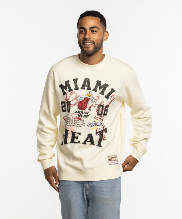 A man smiles against a plain white background, wearing the Mitchell & Ness Miami HEAT 2006 Championship Crewneck by Mitchell & Ness.