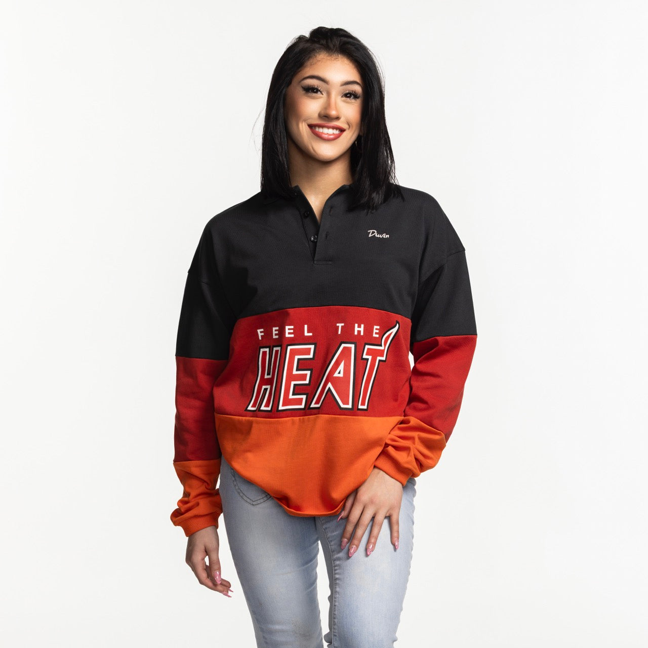 A dark-haired woman smiles in a Court Culture x Duvin Rugby Polo, a relaxed-fit long-sleeve shirt with black, red, and orange color blocks and 