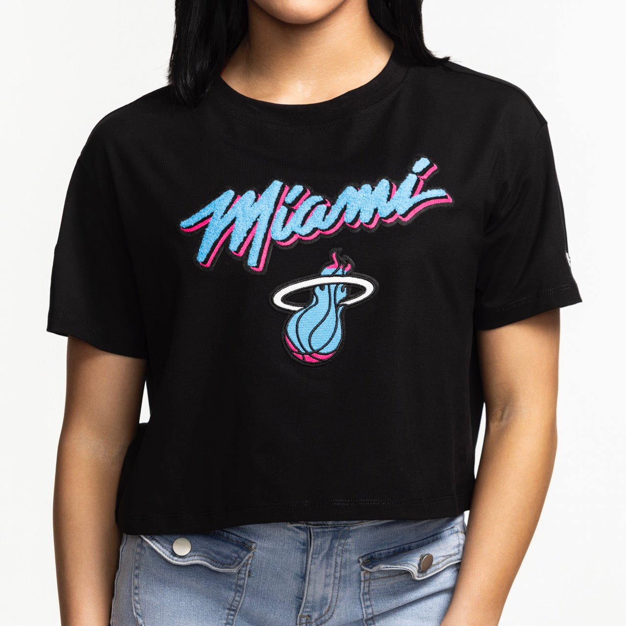 A person wears the Pro Standard Miami HEAT Original Vice Nights Women's Boxy Tee by Pro Standard, a black cropped relaxed fit top with blue and pink 