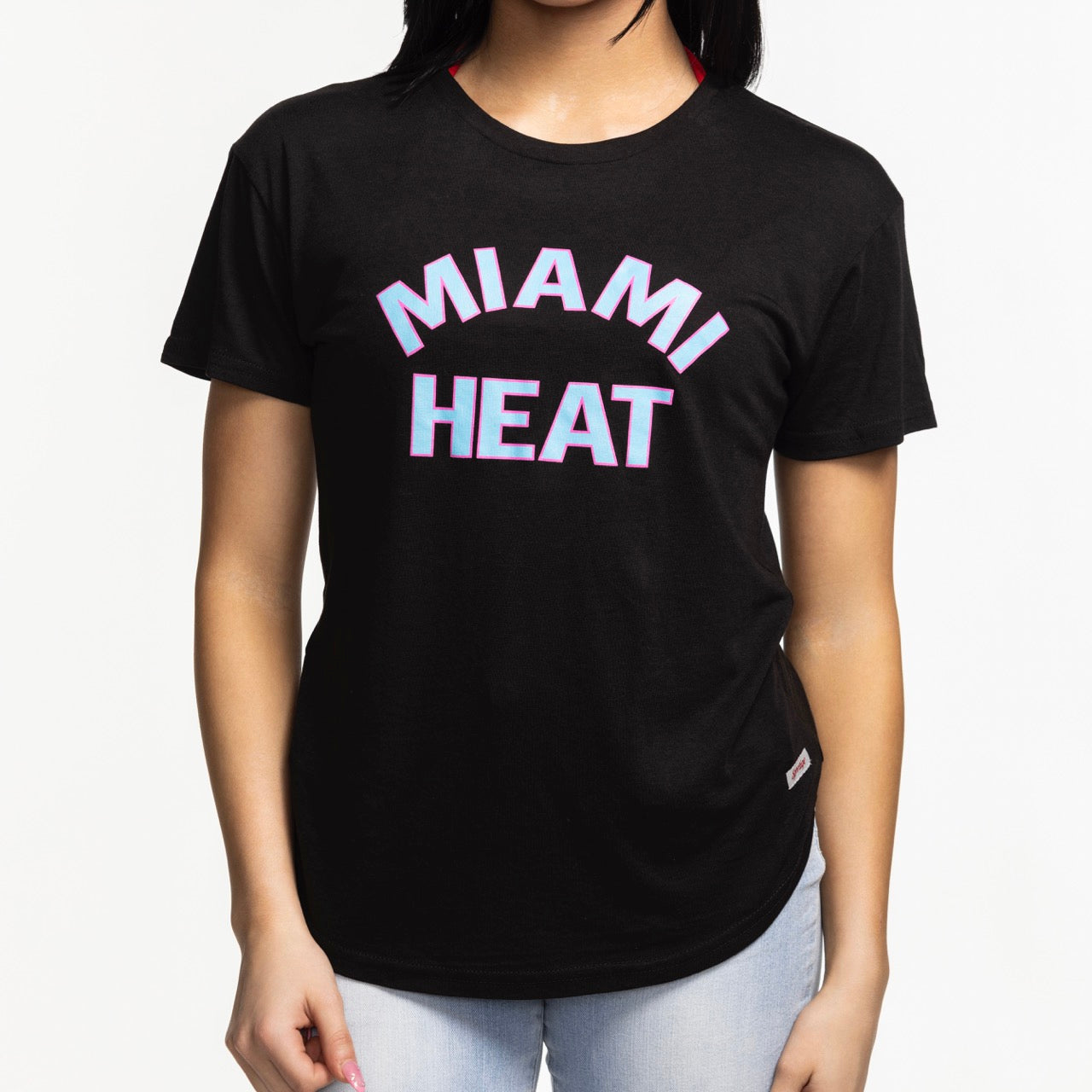 A person wearing the Sportiqe Miami HEAT Original Vice Nights Phoebe Women's Tee—a black cotton T-shirt with bold white and pink outlined 