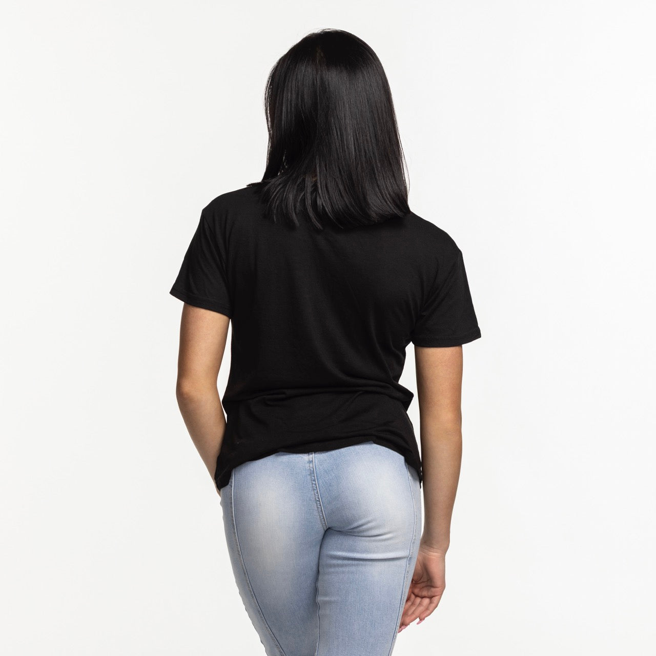 A woman with straight dark hair, wearing the Sportiqe Miami HEAT Original Vice Nights Phoebe Women's Tee by Sportiqe and light blue jeans, stands facing away from the camera against a plain white background.