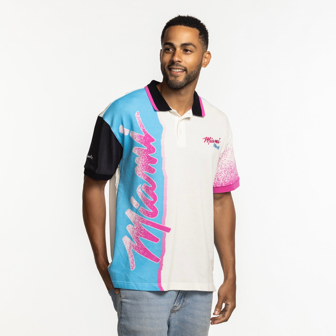A man wears the Court Culture x Duvin Sideline Polo by Court Culture, featuring short sleeves, blue, pink, and black accents, and 