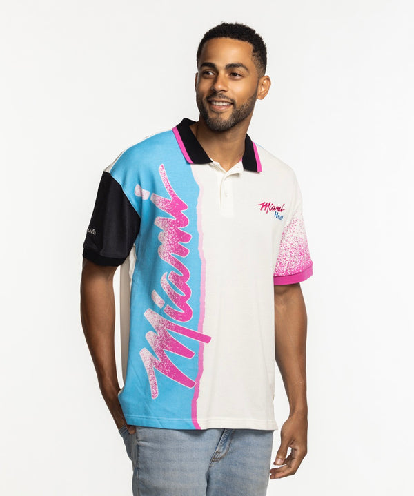 A man wears the Court Culture x Duvin Sideline Polo by Court Culture, featuring short sleeves, blue, pink, and black accents, and 