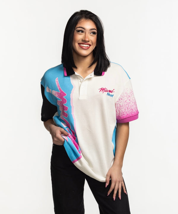 A man wears the Court Culture x Duvin Sideline Polo by Court Culture, featuring short sleeves, blue, pink, and black accents, and 