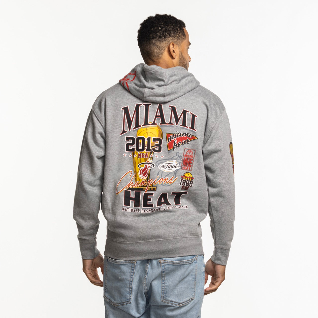 A man faces away in a Mitchell & Ness Miami HEAT 2013 Champions Hoodie, standard fit in gray cotton-poly blend, with vibrant graphics and text celebrating the team's NBA win plus logos and championship years on the back. Machine wash cold.