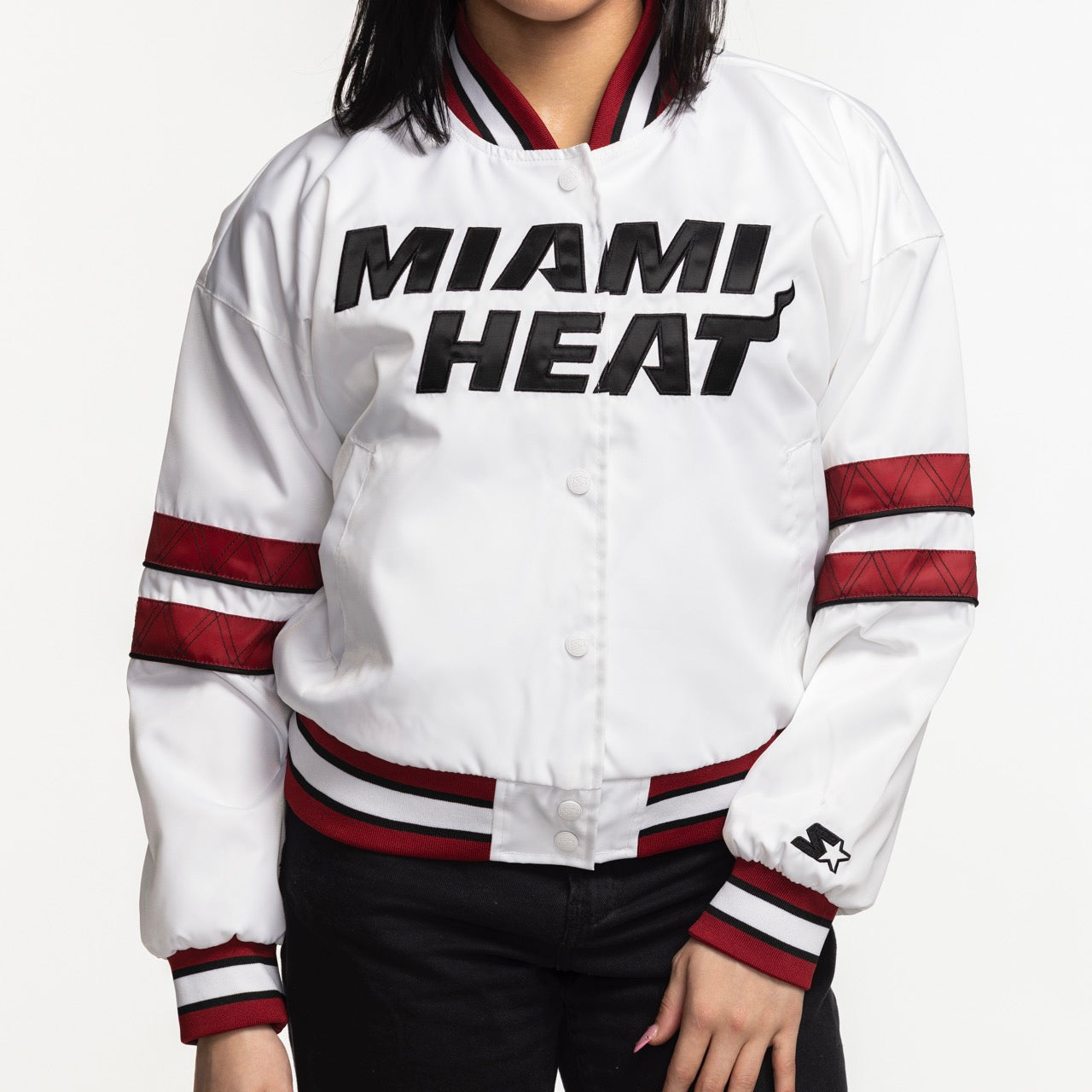 A woman wears the G-III Sports Miami HEAT Interception Women's Jacket—standard fit, white polyester with red and black striped sleeves and collar, MIAMI HEAT in bold black letters on the front, by G-III Sports. Machine washable.
