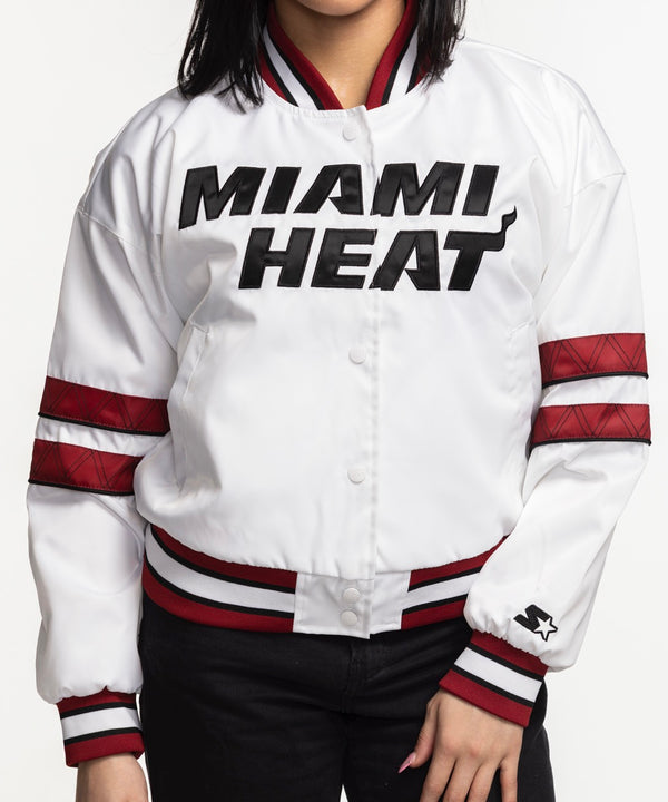 A woman with straight black hair stands against a white background wearing the G-III Sports Miami HEAT Interception Women's Jacket in white with red accents, black pants, and gold hoop earrings. She faces forward with her hands in the jacket pockets.