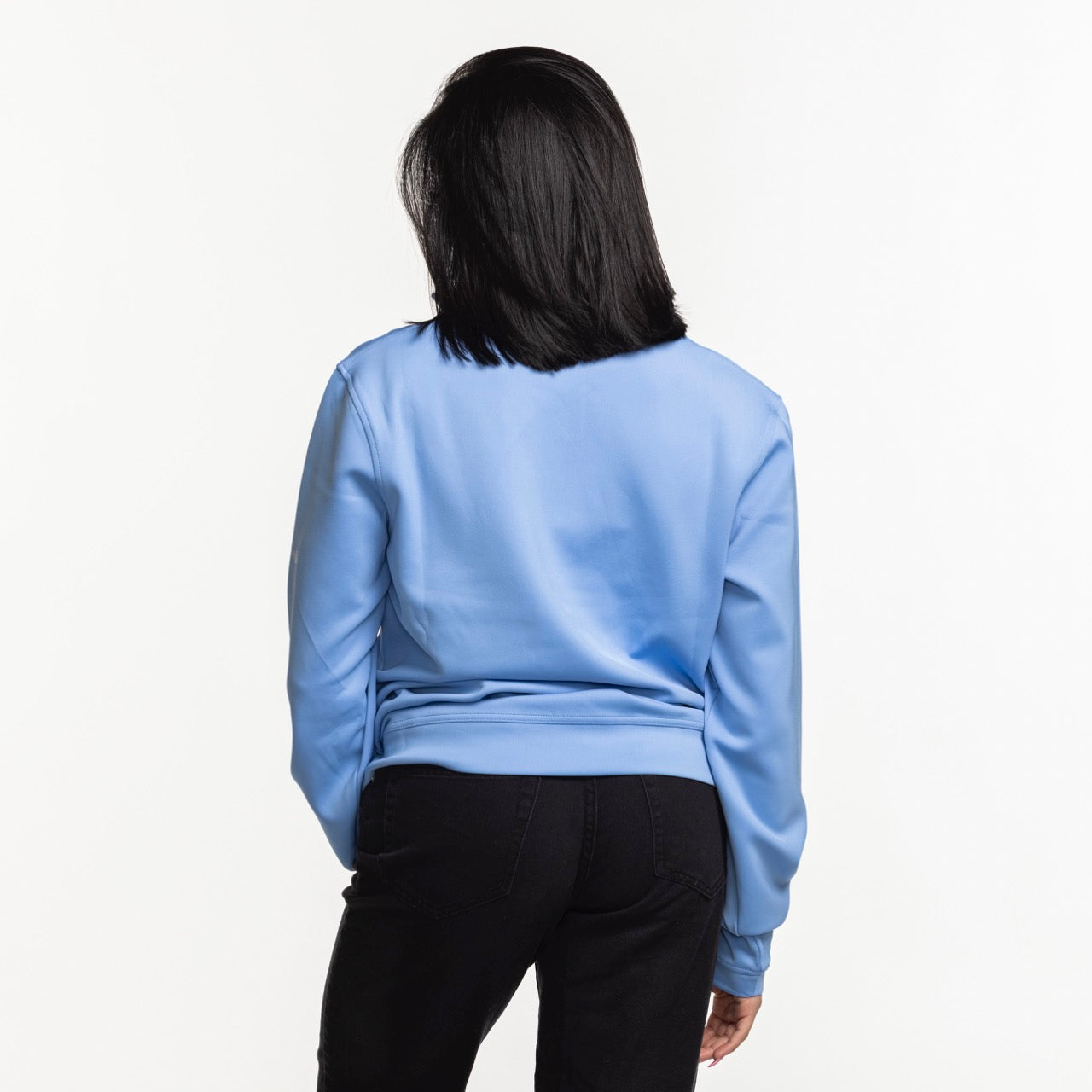A woman with shoulder-length dark hair stands with her back to the camera, wearing the Columbia Miami HEAT Original Vice Nights Women's 1/4 Zip by Columbia Outdoor and black pants against a plain white background.